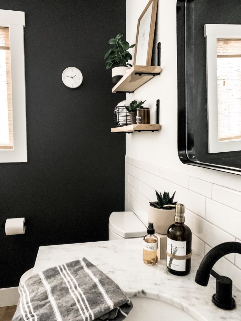 bathroom with black wall, tile. and wood shelves above toilet