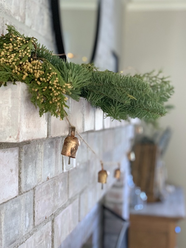 pine and brass bell garland on brick fireplace