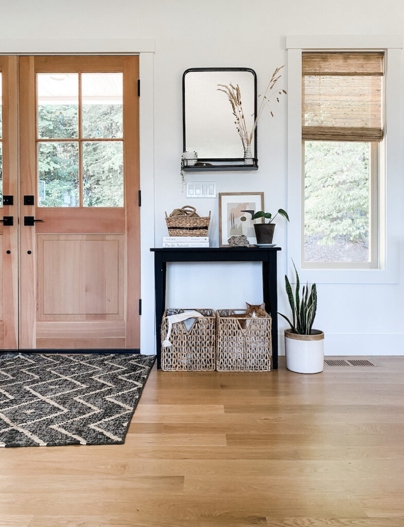 entryway with rug, table, baskets, and mirror