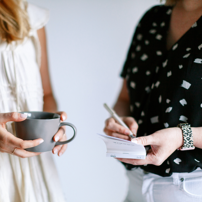 two women talking with notepad and coffee cup