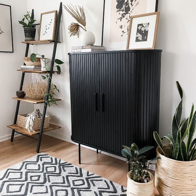 room with bookshelf and black cabinet with plants, artwork, and baskets.