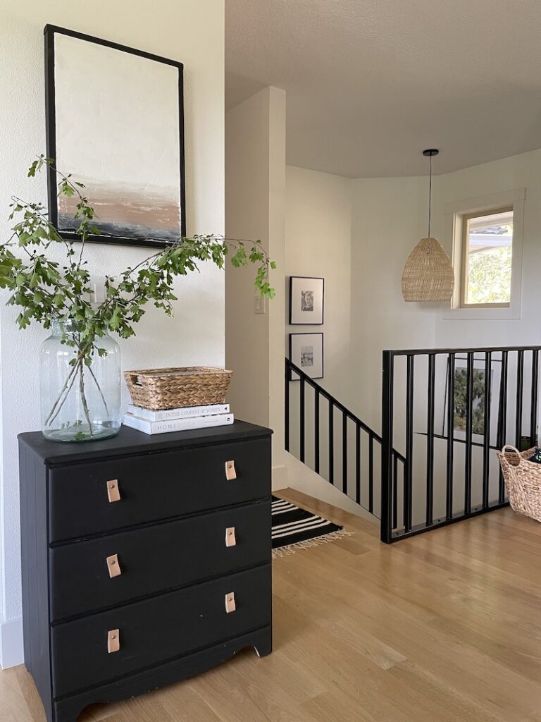 organic modern hallway with black metal railing and black painted dresser with books, vases, and baskets