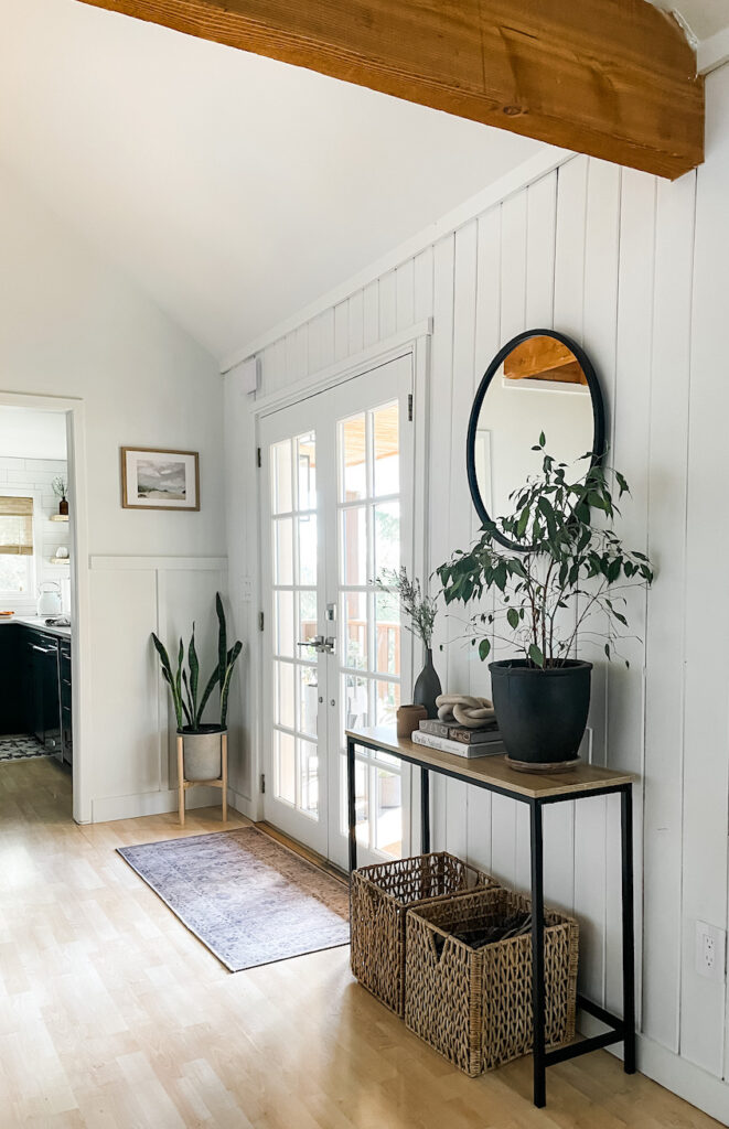 round mirror in entryway with console table, baskets, and rug