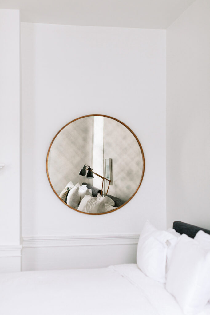 white bedroom with round wall mirror