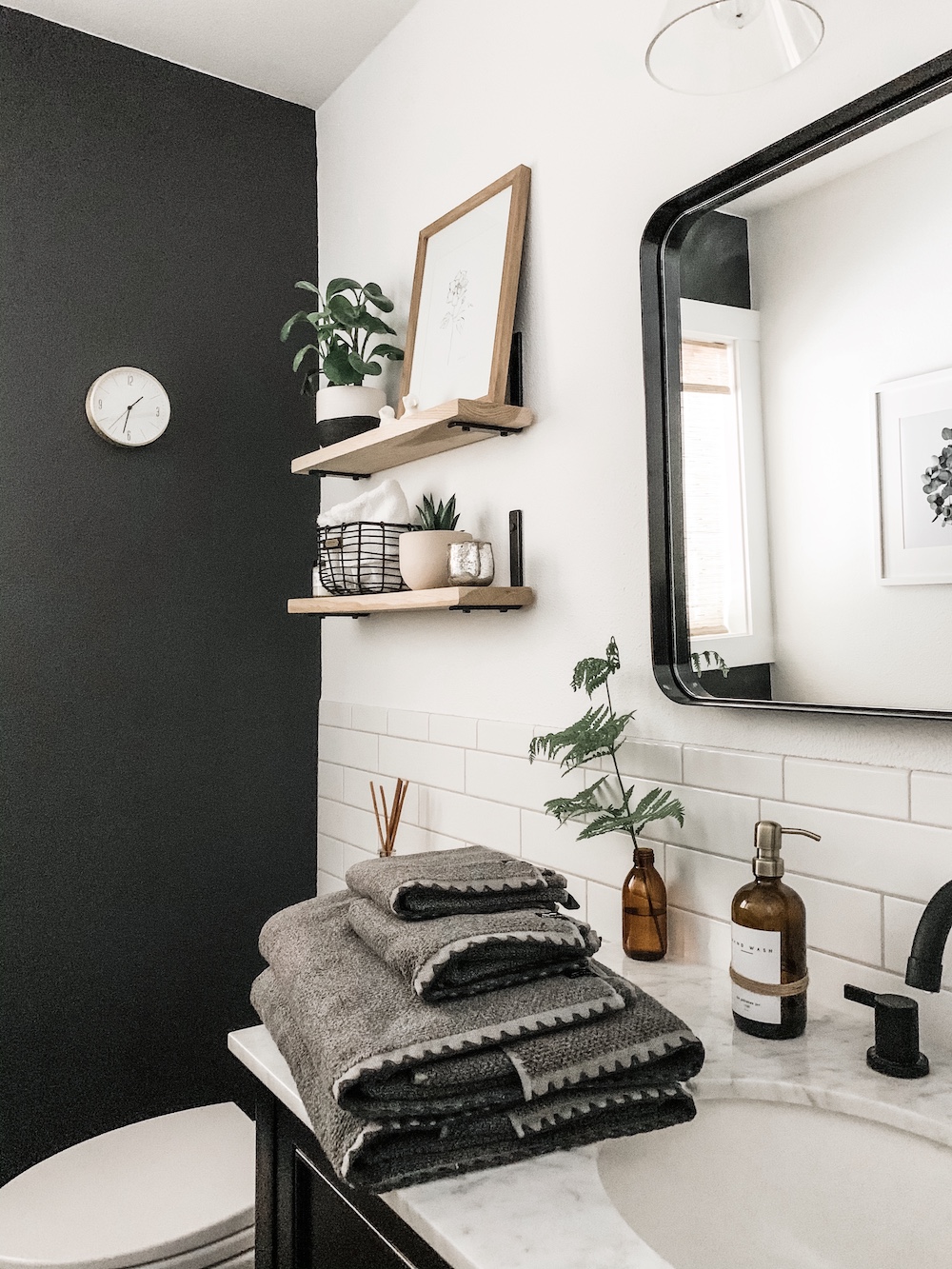 bathroom with black wall and white tile with wood shelves above toilet
